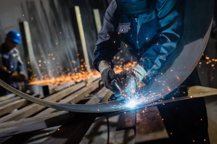 Man using welding torch to cut metal sheet in workshop.