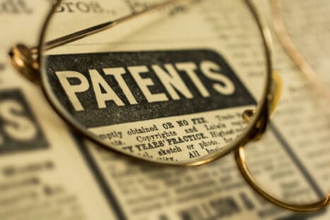 The word, Patents, on an old newspaper with antique gold glasses.